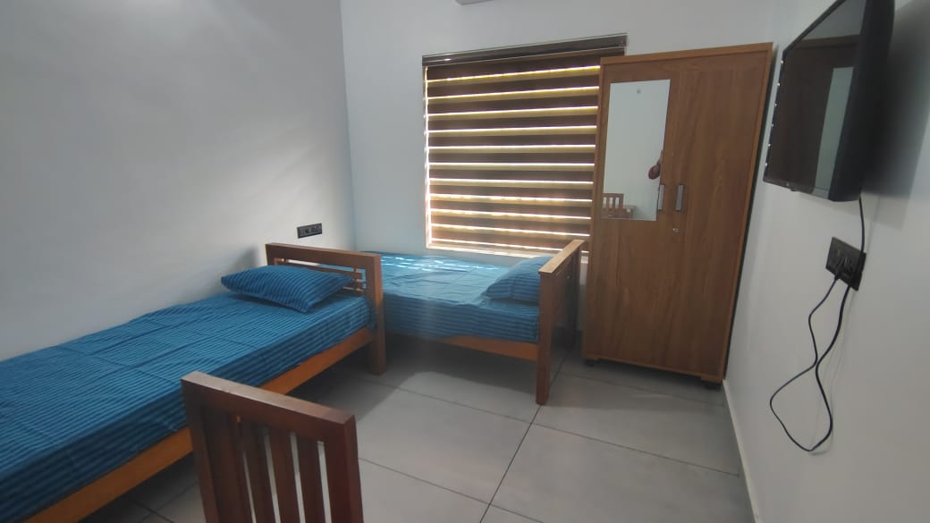 A patient room with two beds, wardrobe and window blinds