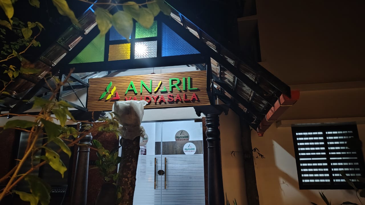 The lit Anaril Vaidyasala entrance at night, under its stained-glass canopy